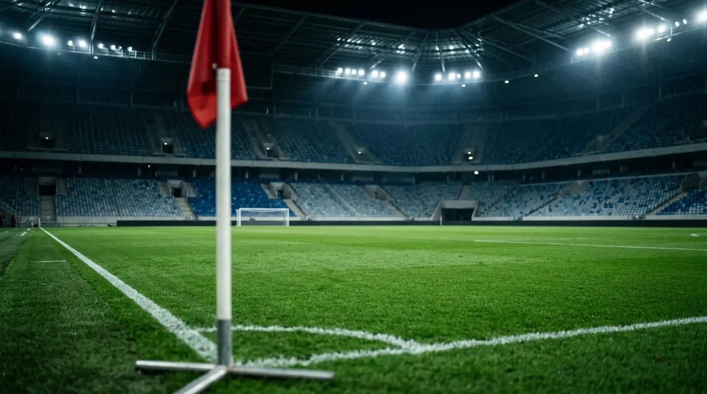Grüner Rasen unter einem geschlossenen Stadiondach mit kühlem Flutlicht, im Vordergrund unscharf ein Fragment der Eckfahne, dahinter leere, weiche Ränge – Spannung vor einem grossen Halbfinal.