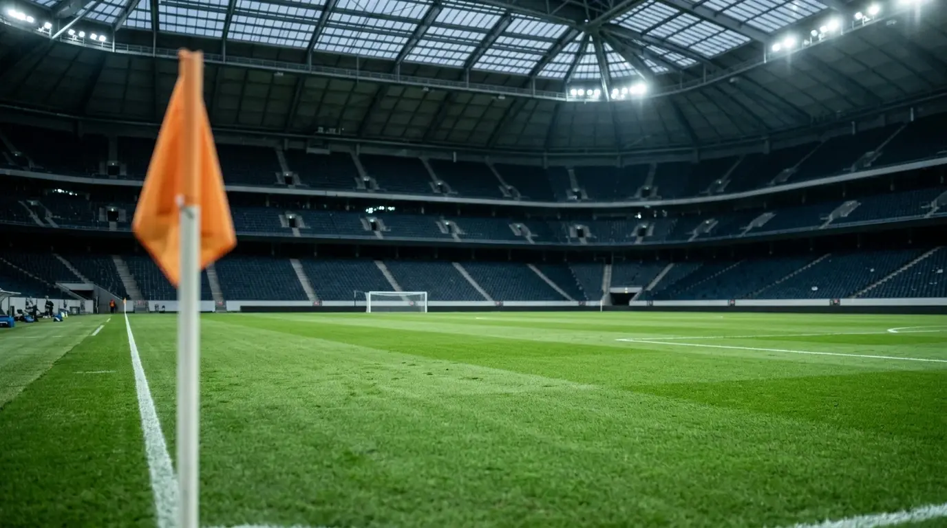 Grüner Rasen unter geschlossenem Stadiondach mit kühlem Kunstlicht, im Vordergrund unscharf die Eckfahne, im Hintergrund leere Ränge – ruhige Anspannung vor einem grossen Halbfinal.